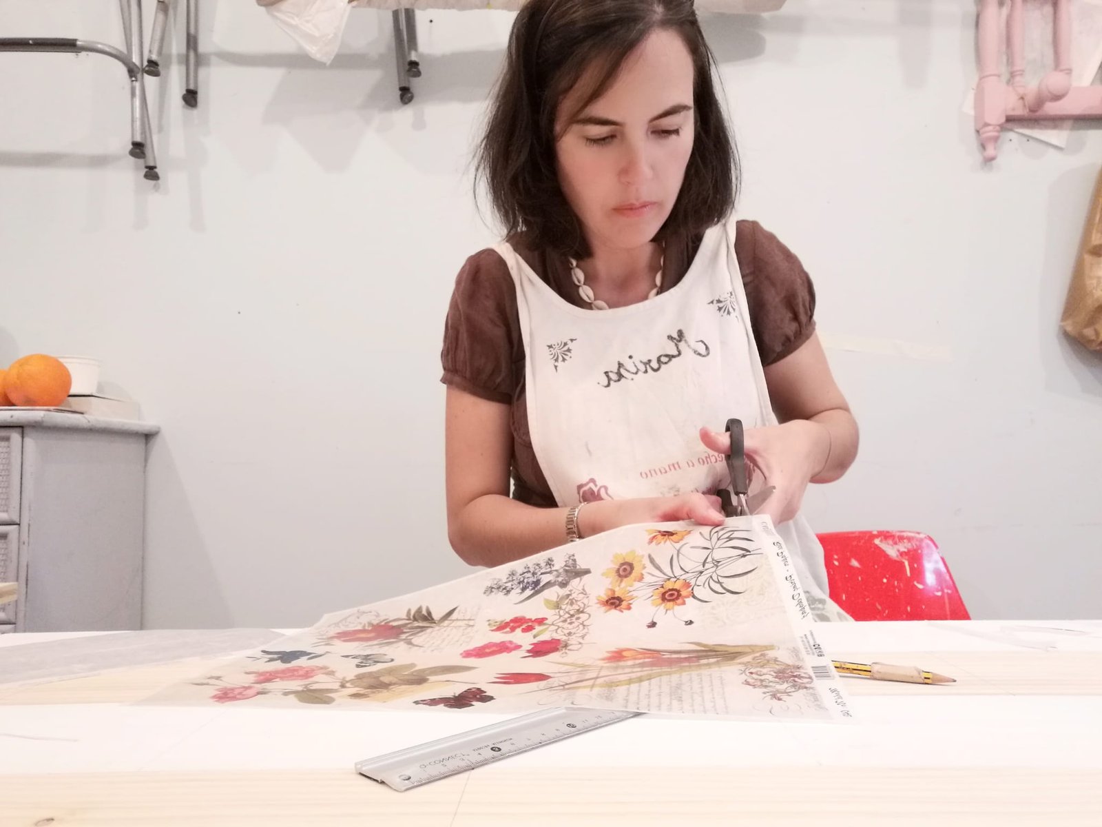 Mujer concentrada cortando una lámina decorativa con tijeras, en una mesa con reglas y lápices.